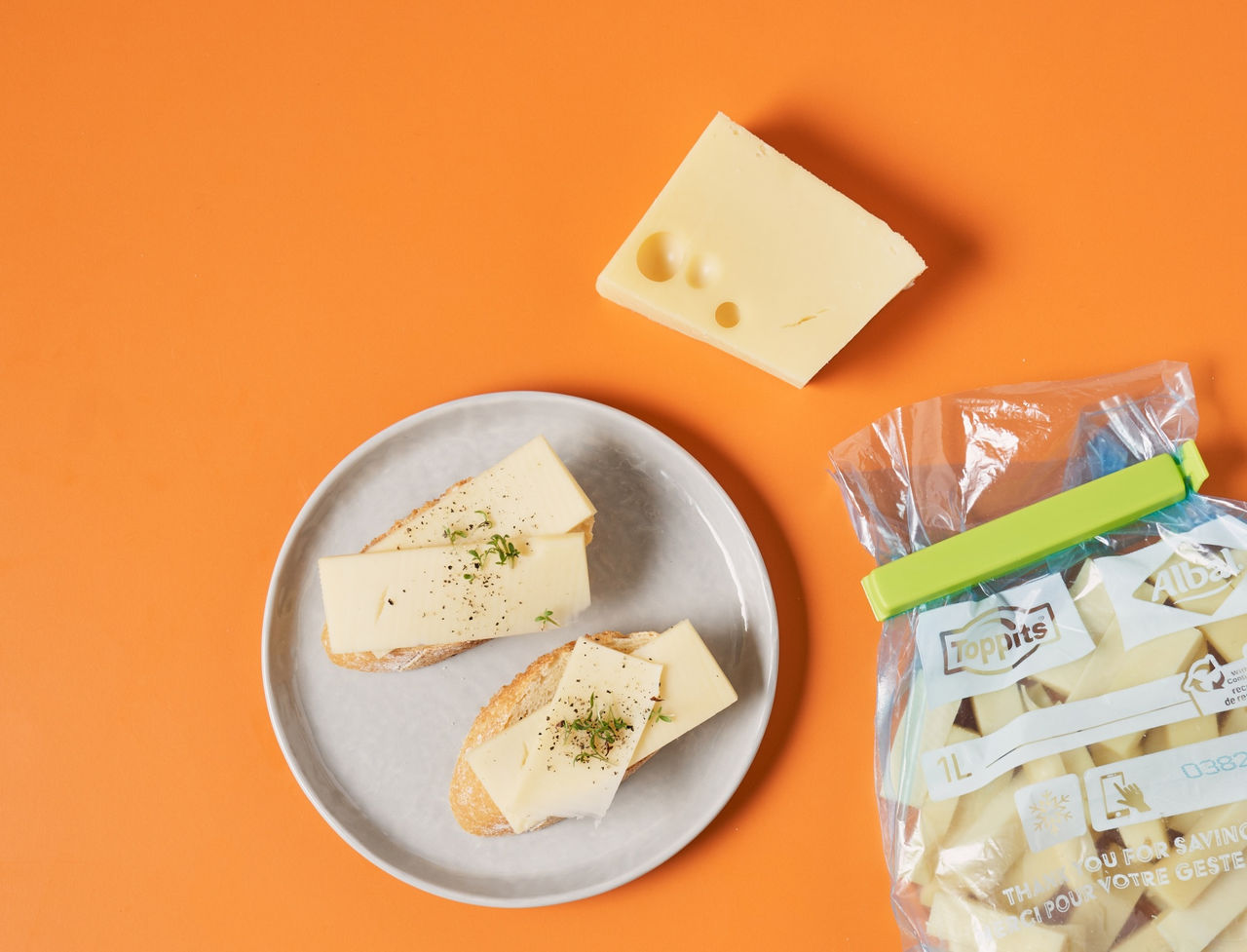 Scheiben Käse auf Brot, daneben ein Stück Käse und ein verschlossener Toppits Beutel.